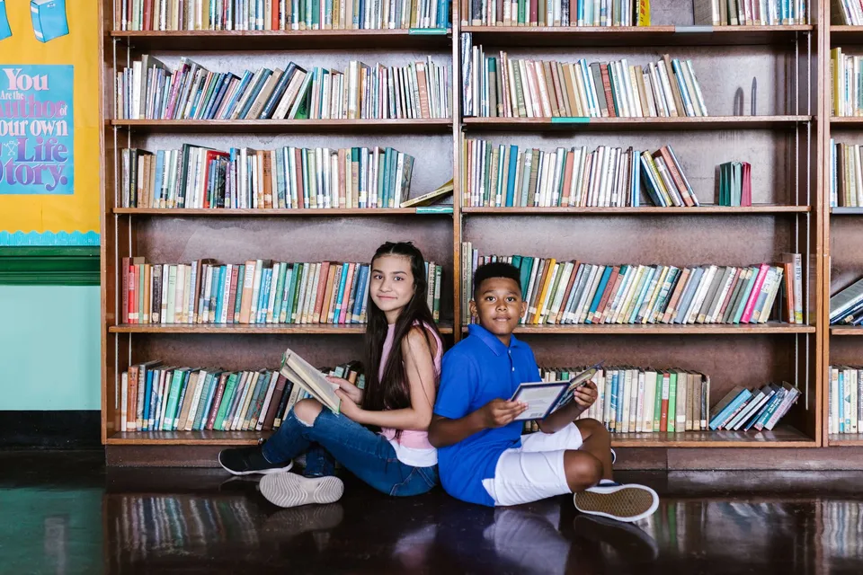 Two children reading books in a school library, fostering learning and diversity.